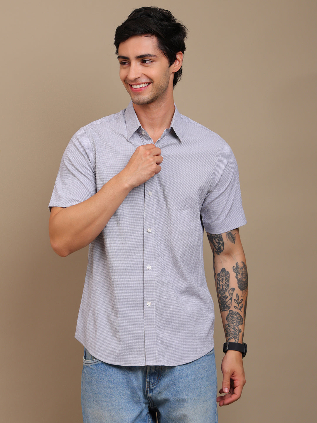 Man wearing a light gray short-sleeve shirt and blue jeans against a beige background