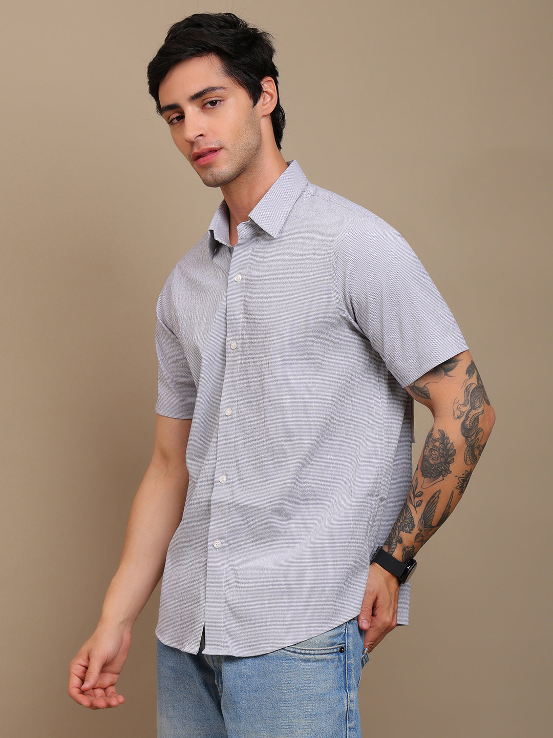 Man wearing a light gray short-sleeve shirt and jeans against a beige background