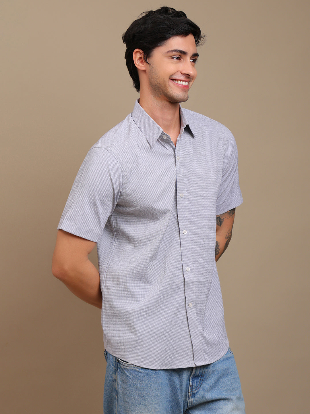 Man wearing a light gray short-sleeve shirt and blue jeans on a beige background