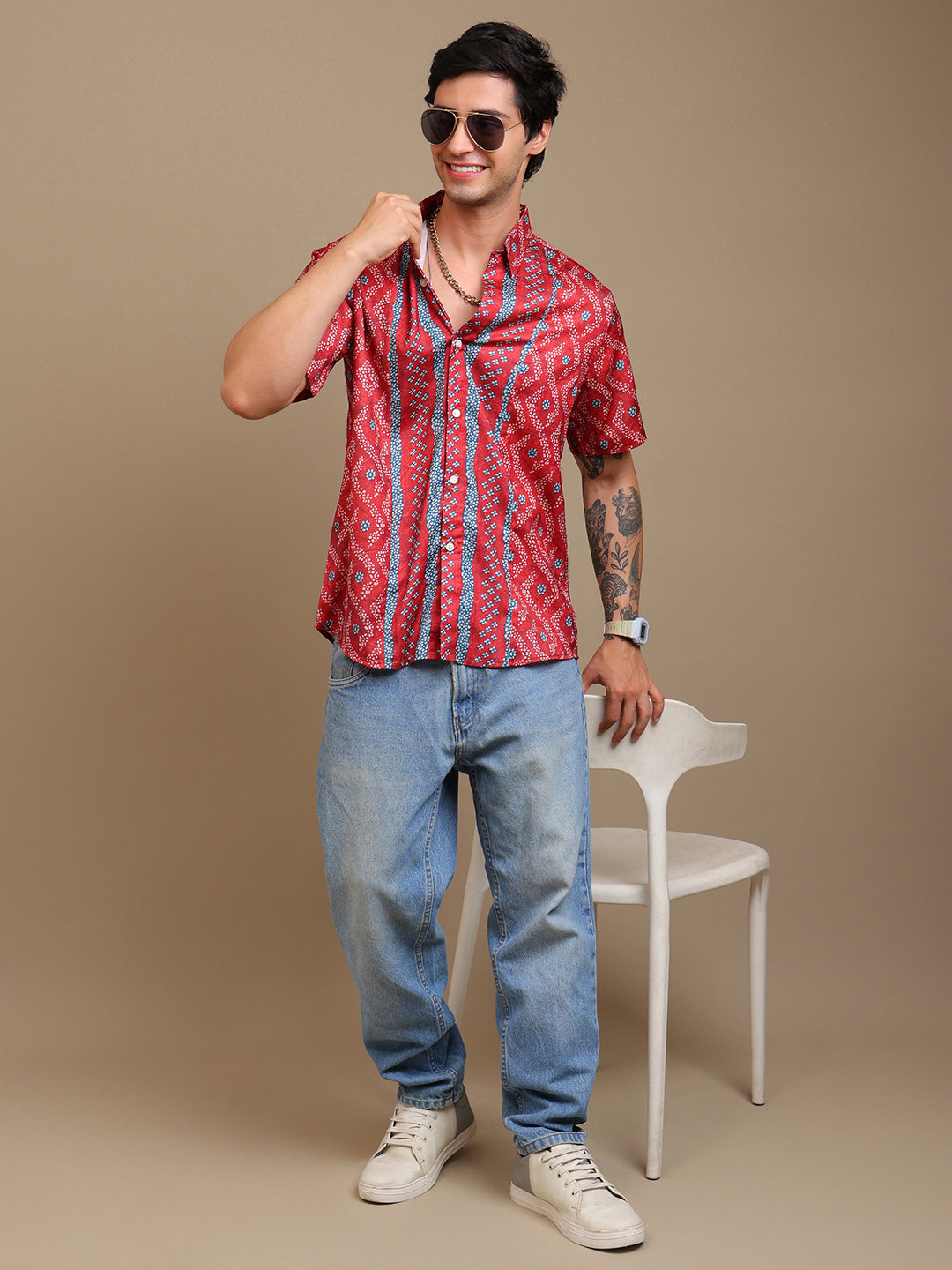 Man wearing a red patterned shirt and blue jeans posing against a beige background