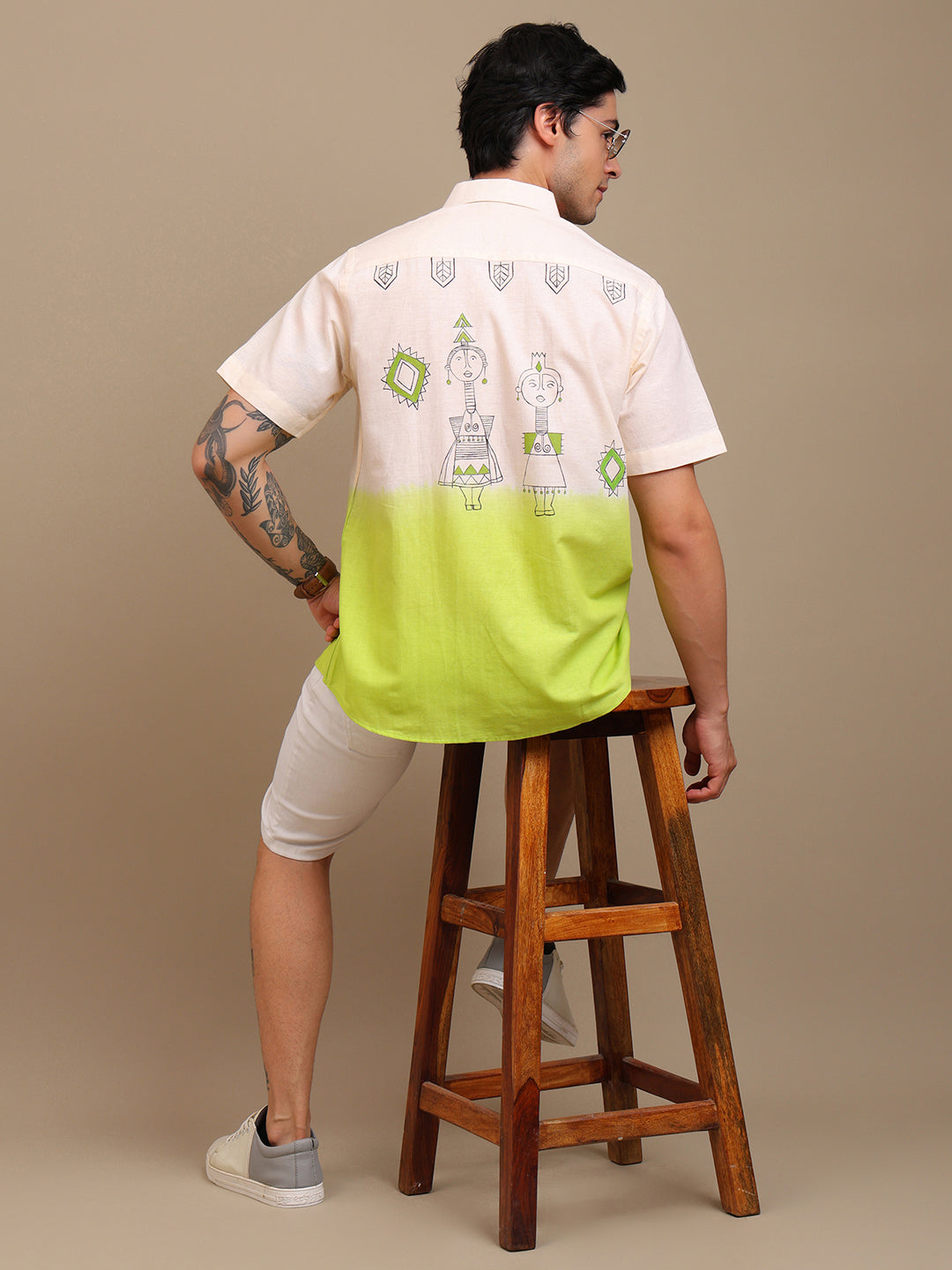 Person wearing a shirt with a unique design, standing on a wooden stool against a beige background